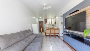 A living room with a grey sofa, a flat-screen TV mounted on a blue wall, and a ceiling fan. - Apto bem Localizado a 500mts da Praia Rhi206 (Florianópolis)
