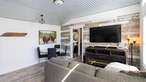 A modern living room with a large flat-screen TV, a gray sofa, and a dining area with a small table and chairs. - Bison View Secluded Cabin for 6 w/ Hot Tub on Wildlife Sanctuary (Johnson City)
