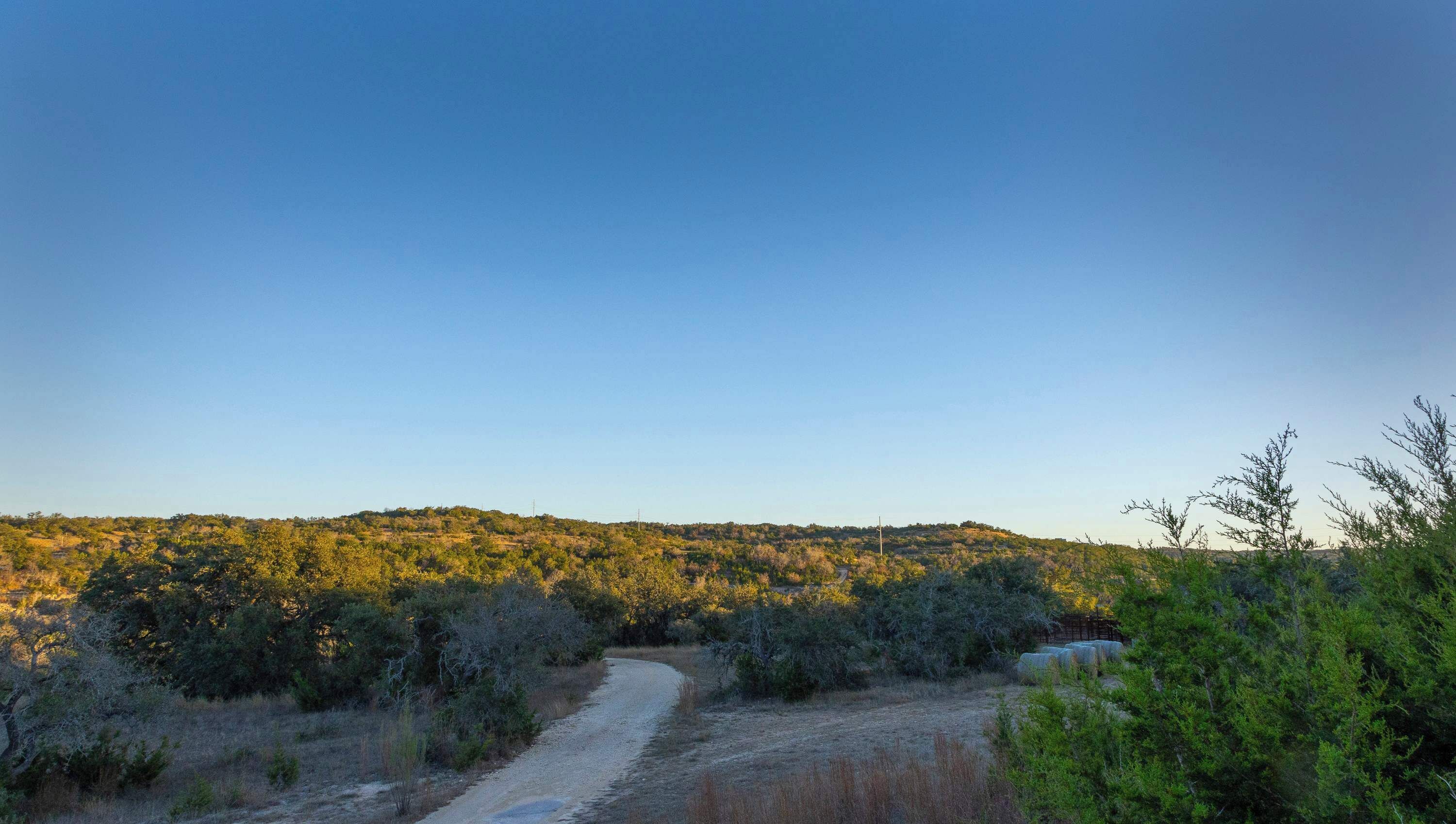 A dirt path leading through a hilly landscape with sparse vegetation and a clear sky.