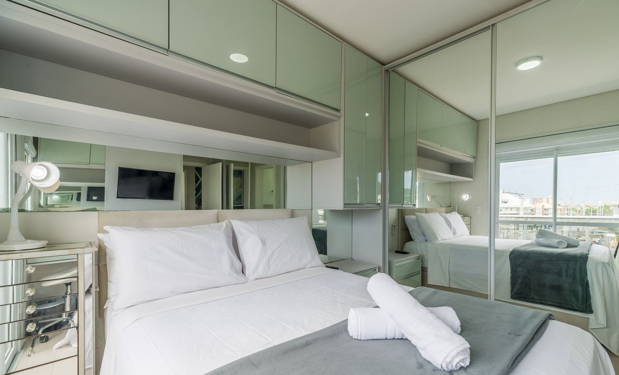 Habitación de hotel moderna con una cama grande, un escritorio con lámpara, televisión y un ventanal con vistas a la ciudad.