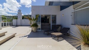 A modern building with a tiled exterior, a covered patio area with outdoor furniture, and a large potted plant. - Apartment w/ Barbecue 160m From the Beach Rgl0304 (Florianópolis)