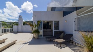 Un edificio moderno con fachada de azulejos, un patio cubierto con mobiliario exterior y una planta grande en maceta.