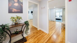 Un couloir doté d’un plancher en bois, un tableau représentant la Joconde accroché au mur, une pancarte indiquant « Meilleur endroit où vivre », et une petite plante posée sur une console.