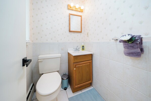 A small bathroom with a toilet, sink, and a mirror with lights above.