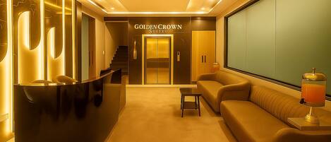 A reception area with a reception desk, a sofa, a small table, and a drink dispenser. There is a staircase leading to the Golden Crown Suites.