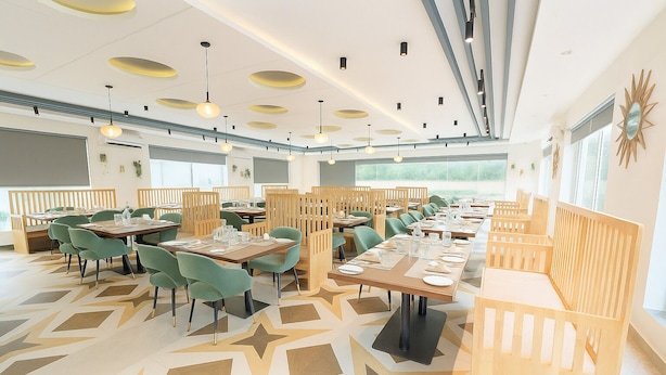 A modern dining area with wooden partitions, green chairs, and a geometric patterned floor. - Golden Crown Suites (Anekal)