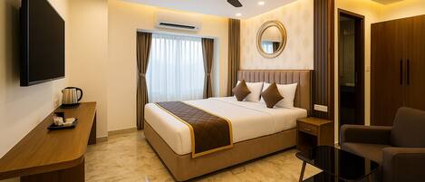 A hotel room with a bed, a desk, a chair, a TV, an air conditioning unit, and a ceiling fan.