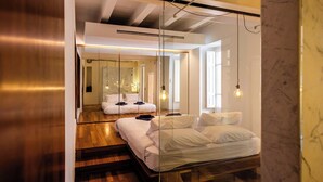 Un dormitorio moderno con un panel de vidrio, piso de madera y una cama con ropa blanca.