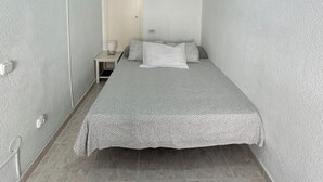 Une petite chambre à coucher, bien rangée, avec un lit, une table de chevet et un luminaire fixé au mur.