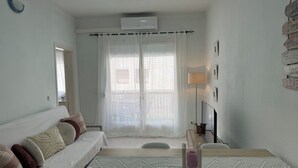 Une chambre moderne et bien éclairée, avec un lit, une table de chevet dotée d’une lampe et une fenêtre ornée de rideaux légers.