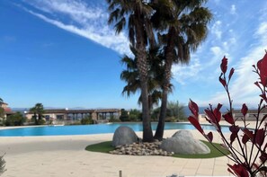 Uma área de piscina com palmeira, pedras e céu azul límpido.