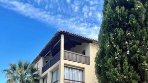 Un bâtiment à deux étages doté d’un balcon, d’un mur en pierre et d’un grand arbre.