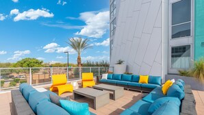 A rooftop terrace with blue and yellow outdoor furniture, a palm tree, and a view of the cityscape. - Cozy Green 1BR Retreat Pool, Hot Tub & Near ASU & Mill Ave (Tempe)