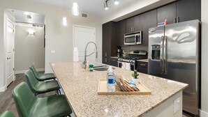 A modern kitchen with a granite countertop, stainless steel appliances, and green bar stools. - Cozy Green 1BR Retreat Pool, Hot Tub & Near ASU & Mill Ave (Tempe)