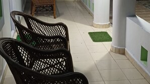 Un corridoio con pareti bianche, elementi decorativi verdi e pavimento piastrellato. Si notano due poltrone in vimini e una finestra con zanzariera.