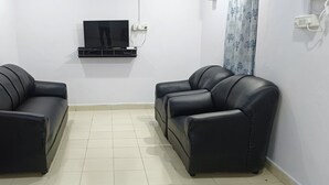 Una stanza con due divani in pelle nera, una TV a schermo piatto fissata al muro e un pavimento piastrellato.