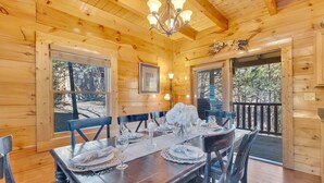 A wooden cabin with a dining table set for six, surrounded by chairs, and a chandelier above.