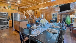 A log cabin interior with a dining area set for a meal, wooden floors, and a stone fireplace.
