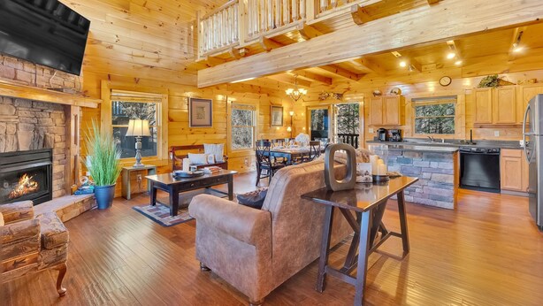 A spacious wooden cabin with a fireplace, a dining area, a kitchen, and a balcony.