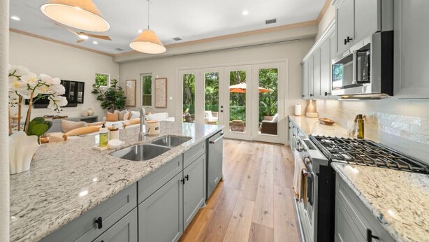 A modern kitchen with granite countertops, stainless steel appliances, and a large window overlooking a garden. - The DOVI Collection | Gated Luxury Retreat & Pool (The Woodlands)