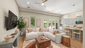 A modern living room with a sectional sofa, a coffee table, and a TV mounted on the wall. - The DOVI Collection | Gated Luxury Retreat & Pool (The Woodlands)