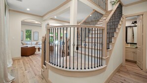 A spacious living area with a curved staircase leading to an upper floor. - The DOVI Collection | Gated Luxury Retreat & Pool (The Woodlands)