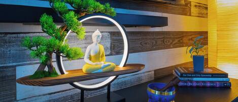 A meditation area with a statue, a small tree, and books on a table.