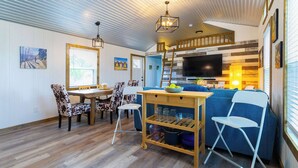 A cozy living area with a dining table, chairs, a sofa, a TV, and a kitchen area. - Shady Grove Tranquil Hill Country Cabin for 8 Near Pedernales Falls (Johnson City)