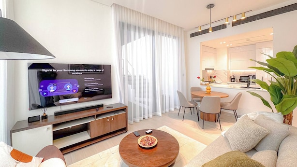 A modern living room with a flat-screen TV, a dining area, and a kitchen in the background. - 2 Bed, Private Pool, Big Terrace, Solysian Stay (Dubai)