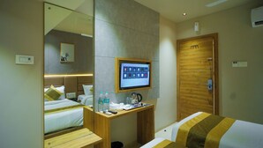 A hotel room with a bed, a desk with a computer monitor, a mirror, and a wooden door. - Hotel Amber Paramount (Mumbai)