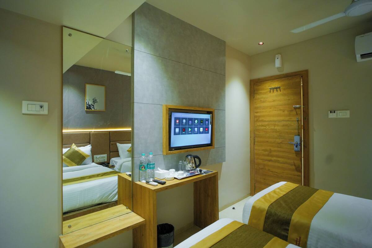 A hotel room with a bed, a desk with a computer monitor, a mirror, and a wooden door.