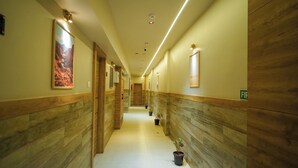 A hotel hallway with wooden paneling, a long corridor, potted plants, and a fire exit sign. - Hotel Amber Paramount (Mumbai)