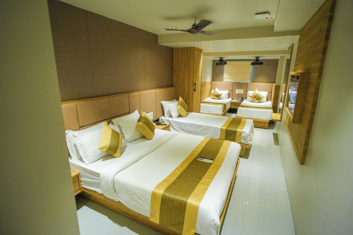 A hotel room with three beds, each with white bedding and gold accents. There is a ceiling fan and a large mirror on the wall.