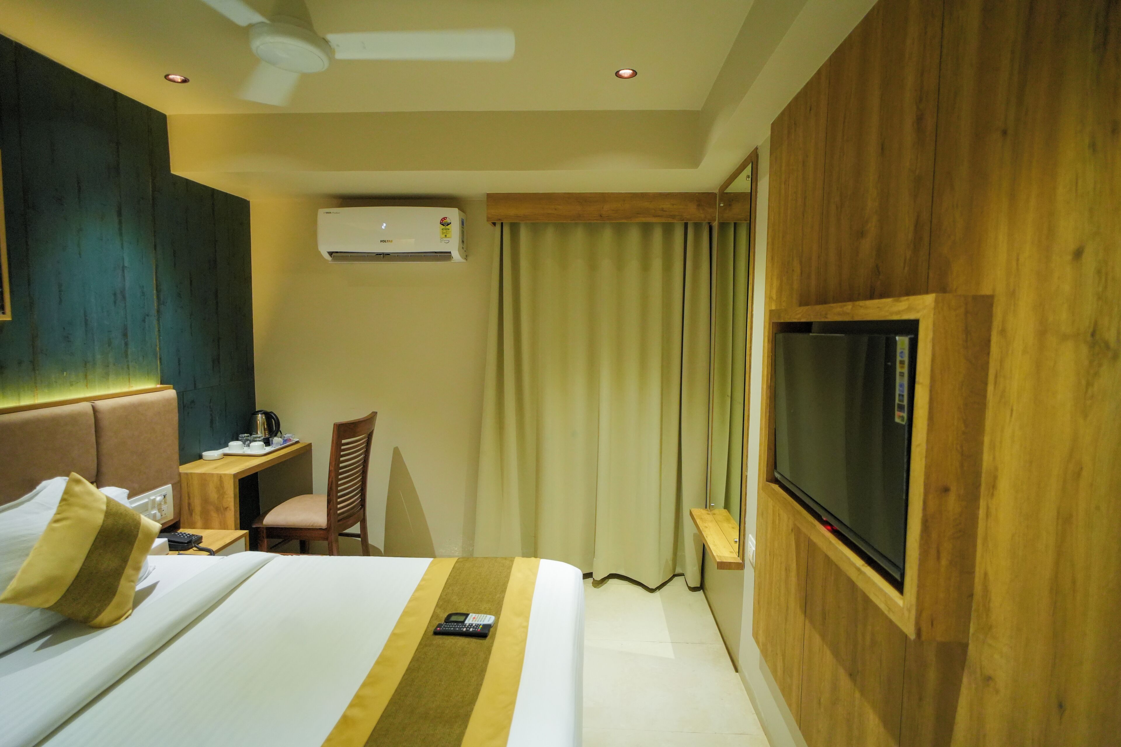 A hotel room with a bed, a desk, a chair, a television, and an air conditioning unit.