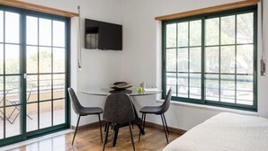 A modern room with a round glass table, two chairs, a bed, and large windows with a view of the outdoors. - Bright Studio with Balcony in Central Cascais (Cascais)