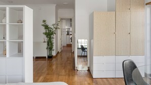 A modern living room with a wooden floor, white shelving units, a large mirror, and a potted plant. - Bright Studio with Balcony in Central Cascais (Cascais)