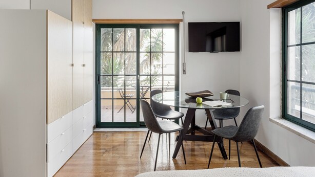 A modern dining area with a glass table, four chairs, and a television mounted on the wall. - Bright Studio with Balcony in Central Cascais (Cascais)