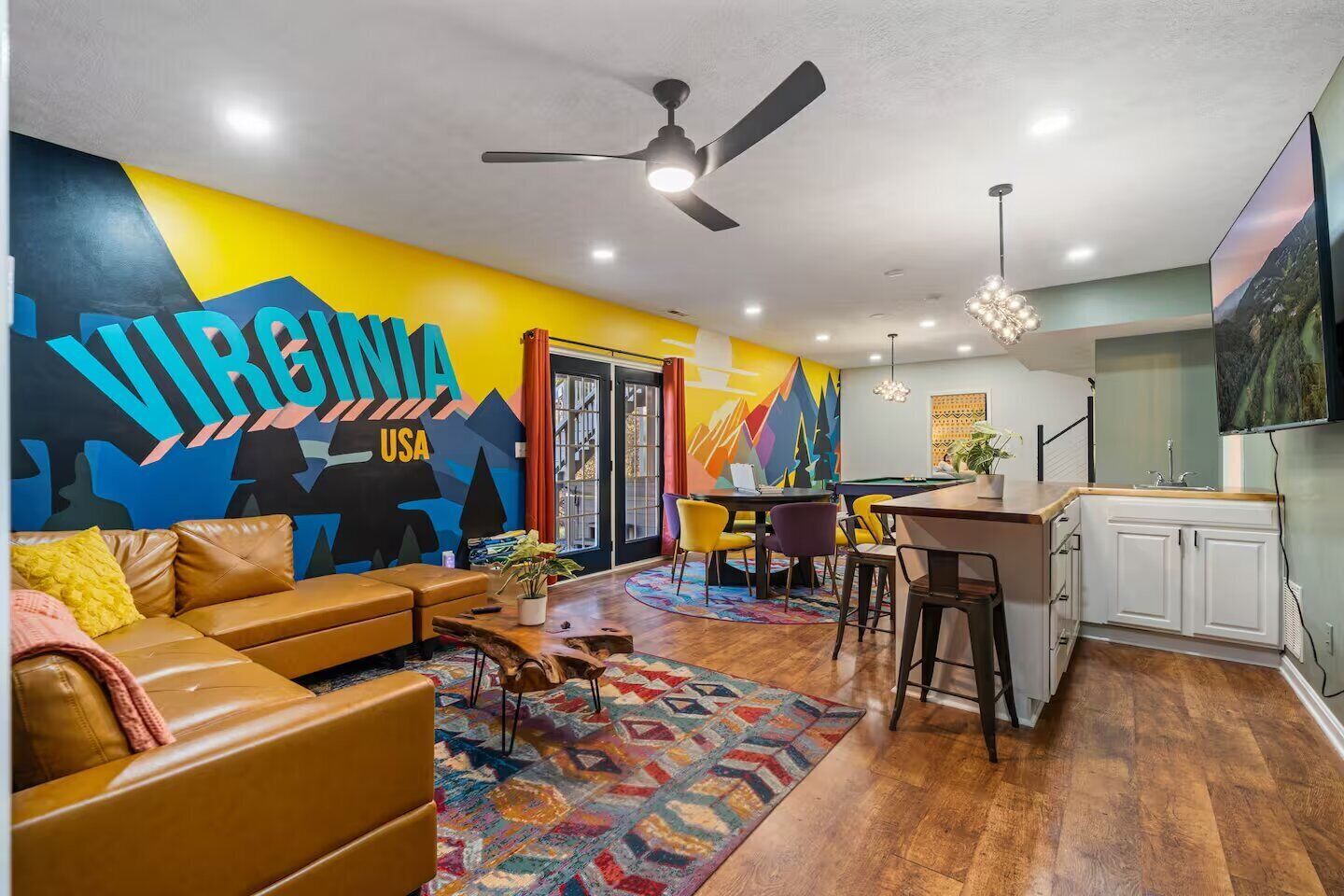 Una sala moderna con un sofá, una mesa de centro y una alfombra colorida. Hay una zona de cocina con barra y una mesa de comedor.
