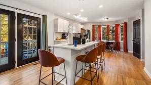 Una cocina moderna con una isla central, taburetes de bar y un comedor con cortinas rojas.