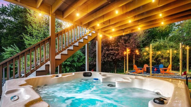 Un jacuzzi con terraza de madera y escaleras, rodeado de árboles y mobiliario exterior.