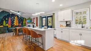Una cocina moderna con armarios blancos, una isla central y un área de comedor con un mural colorido.