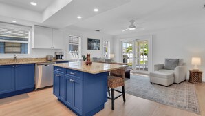 A modern kitchen with blue cabinets, a large island, and a dining area with a white sofa and a side table. - Charming 3-bedroom house in lovely Naples with AC, Pool and Pet Friendly (Naples)