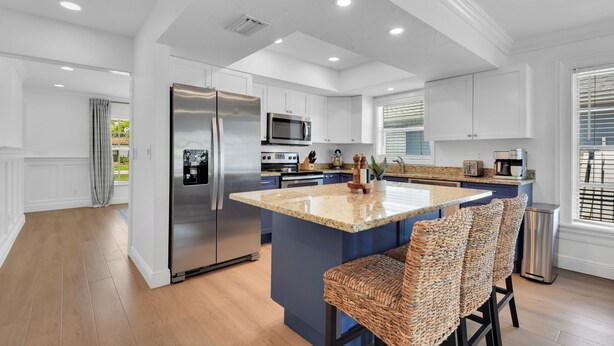A modern kitchen with white cabinetry, stainless steel appliances, and a central island with bar stools. - Charming 3-bedroom house in lovely Naples with AC, Pool and Pet Friendly (Naples)