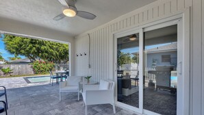 A patio with a pool, white furniture, and a sliding glass door leading to a covered area. - Charming 3-bedroom house in lovely Naples with AC, Pool and Pet Friendly (Naples)
