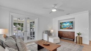 A living room with a sofa, coffee table, and a painting of Naples, Florida. - Charming 3-bedroom house in lovely Naples with AC, Pool and Pet Friendly (Naples)