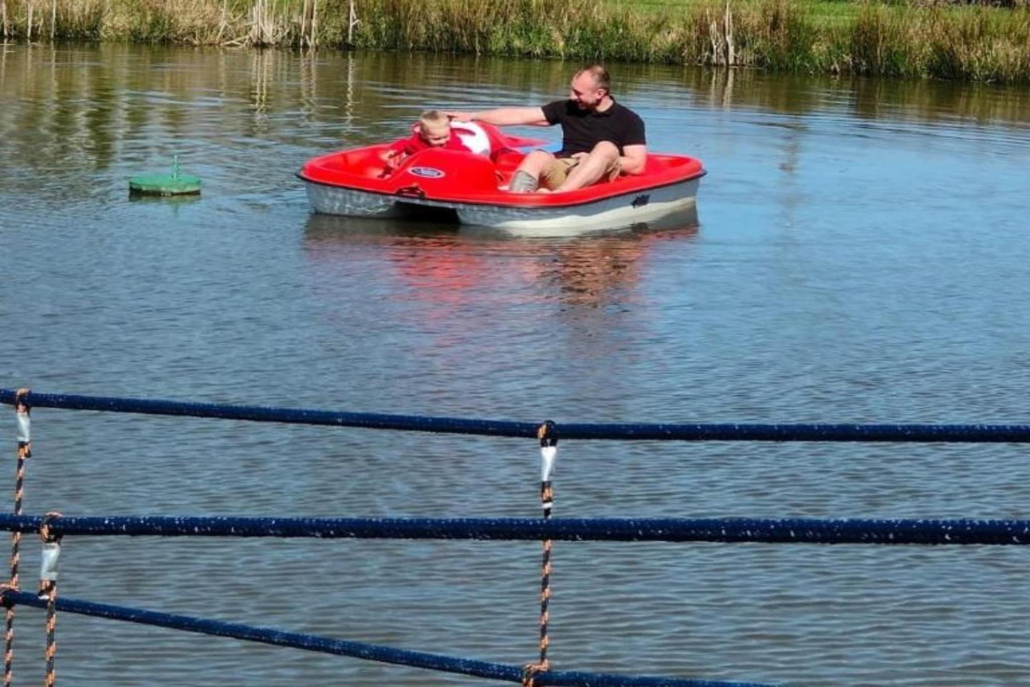 Un homme dans un bateau rouge sur une étendue d’eau calme, avec un quai et des cordes au premier plan.