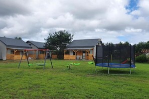 A residential area with two houses, a swing set, a trampoline, and a fenced garden. - Comfortable holiday home, sauna, fishing pond (Wodnica)