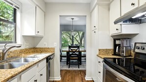 A narrow kitchen with white cabinets, a granite countertop, a built-in oven, and a dining area with a table and chairs. - Lighthouse Tennis Villas: Walk to both Harbor Town, Shops at Sea Pines STR077622 (Hilton Head)