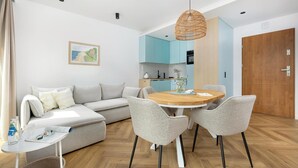 A modern living room with a sofa, a dining table with chairs, a kitchen area, and a wooden door. - Comfortable apartment with a terrace (Trzesacz)