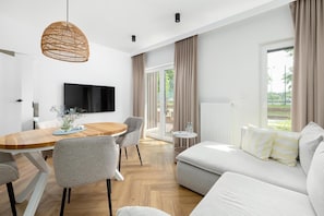 Un salon moderne comprenant un canapé, une table à manger, des chaises, un téléviseur et une grande fenêtre avec des rideaux.